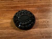 front view of round black faceted stone brooch