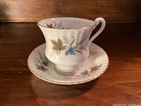 Front view of teacup seated on saucer showing pattern and gold rim