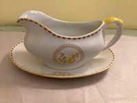 Side view of gravy boat on underplate showing gold dotted rim and motif