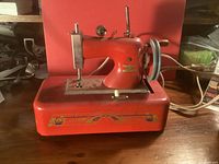 Left side view of red child’s sewing machine showing base decal, needle area and power cord