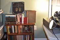 Overall view of three shelves of books on small wooden bookcase with additional books stacked on top