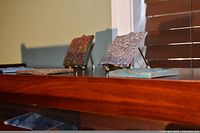 Three tiles displayed on surface, two on brass easels, showing relief and mosaic designs