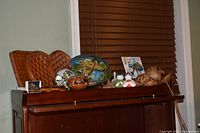 Group view showing woven plates, coconut shell bowl, Greek tile, Japanese bells, carved vessels, wooden spoons on cabinet