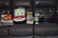 All items laid out on sofa showing binder, carry case, books, card stack, figure cube and storage box