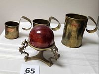 Overall view of three brass milk measures, ornate stand and red sphere