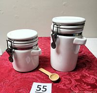 Both white ceramic canisters with wooden spoon