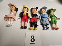 Front view of all five dolls laid side-by-side showing outfits and size reference