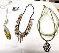 All three necklaces laid out: silver oval pendant, Camille statement, multi-strand green