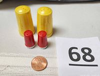 Two yellow bakelite shakers, two red plastic shakers, penny for scale