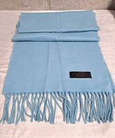 Full view of folded baby blue cashmere scarf showing fringe and label side