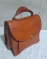Front view of tan leather handbag with flap and twist lock