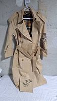 Front view of beige Burberry trench coat with sketch motifs and belt