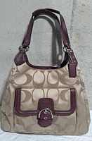 Front view showing signature canvas, burgundy leather trim, flap pocket, hardware