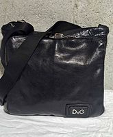 Front view showing polished leather, D&G logo plaque, zip top, adjustable strap