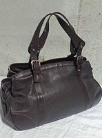 Front and side view of brown pebbled leather handbag with double handles and buckle hardware