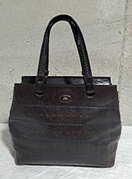 Front view of leather handbag showing structure, handles, logo plaque