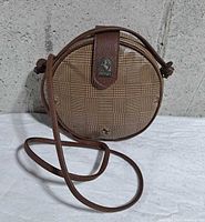 Front view of brown round Ferrari crossbody bag showing badge, pattern and strap