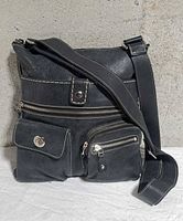 Front view showing overall bag, strap, top zipper and three exterior pockets