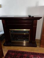 Full view of Dimplex electric fireplace with wood mantel and remotes on top
