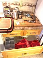 Countertop view showing cannisters, chopping board, utensils, trays, drink carriers in drawer
