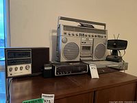 Group view of all six components on cabinet: boombox, wooden clock radio, black clock radio, DVD player, TV antenna, pocket radio