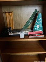 Shelf with Yamaha PortaSound PS-200 keyboard, recorder in sleeve, Wittner metronome box, Olympia harmonica case