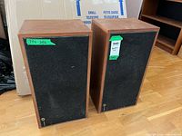 Front view of both speakers with grilles on, showing wood cabinets and size