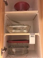 Cabinet shelves with red bowl, two stacked rectangular dishes, two stacked square dishes, lids visible