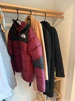 Four coats hanging: North Face puffer, camel coat, dark navy/black coat, grey coat