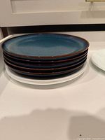 Stack of six blue dinner plates atop white plates