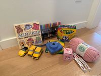 All items grouped on floor including camera, markers, colouring book, yarn, foam cars, novelty box and pens