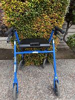 Front view of blue rollator walker showing four wheels, seat, handles, and frame