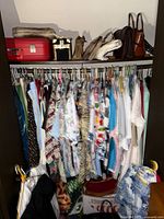 Full closet view showing hanging vintage clothing and top shelf with handbags and luggage