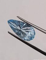 Pear-shaped aquamarine held by tweezers showing face-up starburst cut