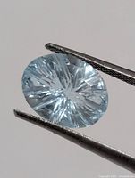 Close-up of aquamarine held by tweezers, showing cut and color