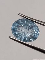 Close-up of oval light blue faceted aquamarine held by tweezers
