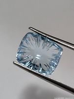 Front view of cushion-cut aquamarine held by tweezers