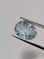 Close-up of oval light-blue aquamarine held by tweezers showing radial faceting