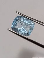 Front view of cushion-cut aquamarine held by tweezers