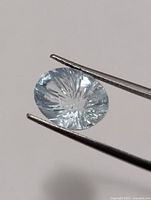 Close-up of aquamarine held by tweezers showing starburst faceting