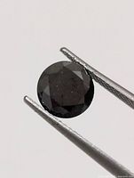 Front view of round black diamond held by tweezers