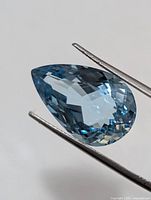 Front view of faceted pear cut blue topaz held by tweezers
