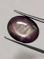 Oval star ruby held by tweezers, displaying color and asterism
