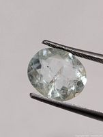 Loose oval green amethyst held by tweezers