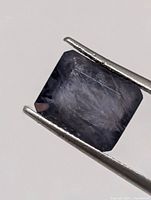 Loose rectangular iolite held by tweezers, front view