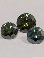 Three loose round brilliant-cut moissanite gemstones showing colour and cut