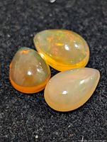 Three pear-shaped opal cabochons showing varied body colors and play-of-color