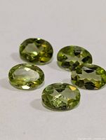 Five oval green peridot gemstones on white background