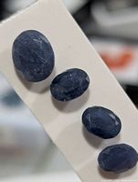 Front view of four loose dark blue oval sapphires on card