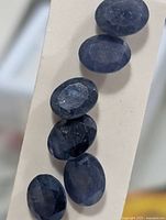 six loose oval faceted blue sapphires on white strip